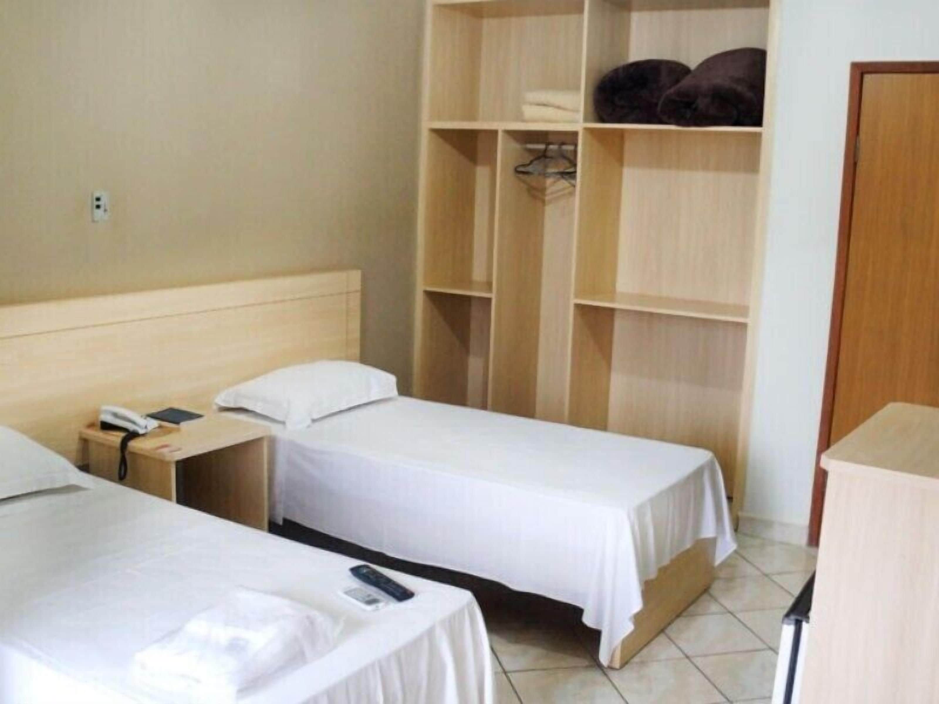 Habitación de hotel con dos camas individuales, un armario de madera y un escritorio con teléfono.