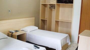 Habitación de hotel con dos camas individuales, un armario de madera y un escritorio con teléfono.