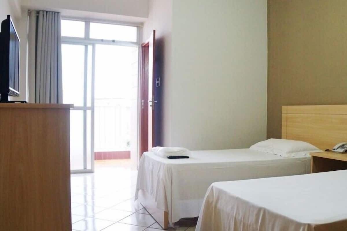 A hotel room with two single beds, a wooden headboard, a desk with a telephone, and a TV on a stand.