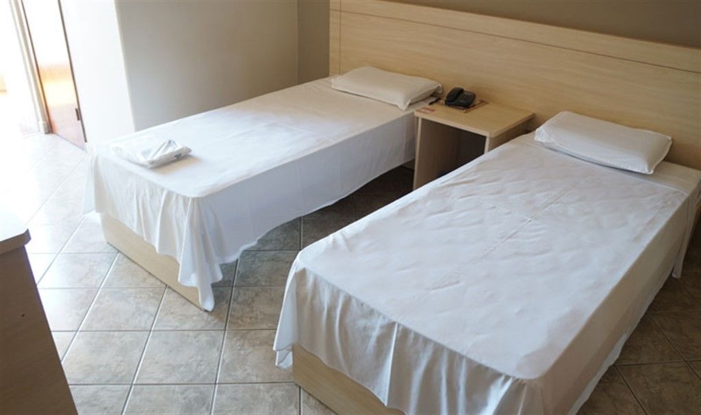 Two single beds with white linens, a bedside table with a phone, and a window with a view.
