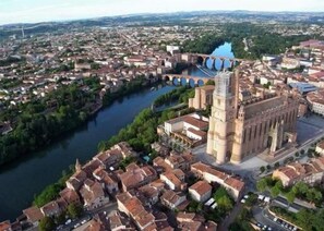 Vista aérea de un pueblo histórico con una iglesia destacada que cuenta con un campanario alto, un río que lo atraviesa y un puente que conecta dos partes del pueblo.