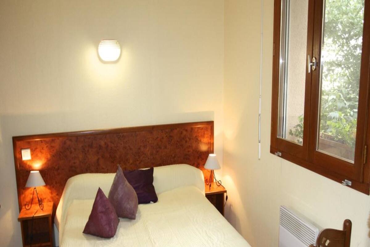 Ein Schlafzimmer mit einem Bett, zwei Nachttischlampen, einem Fenster und einer Heizung.