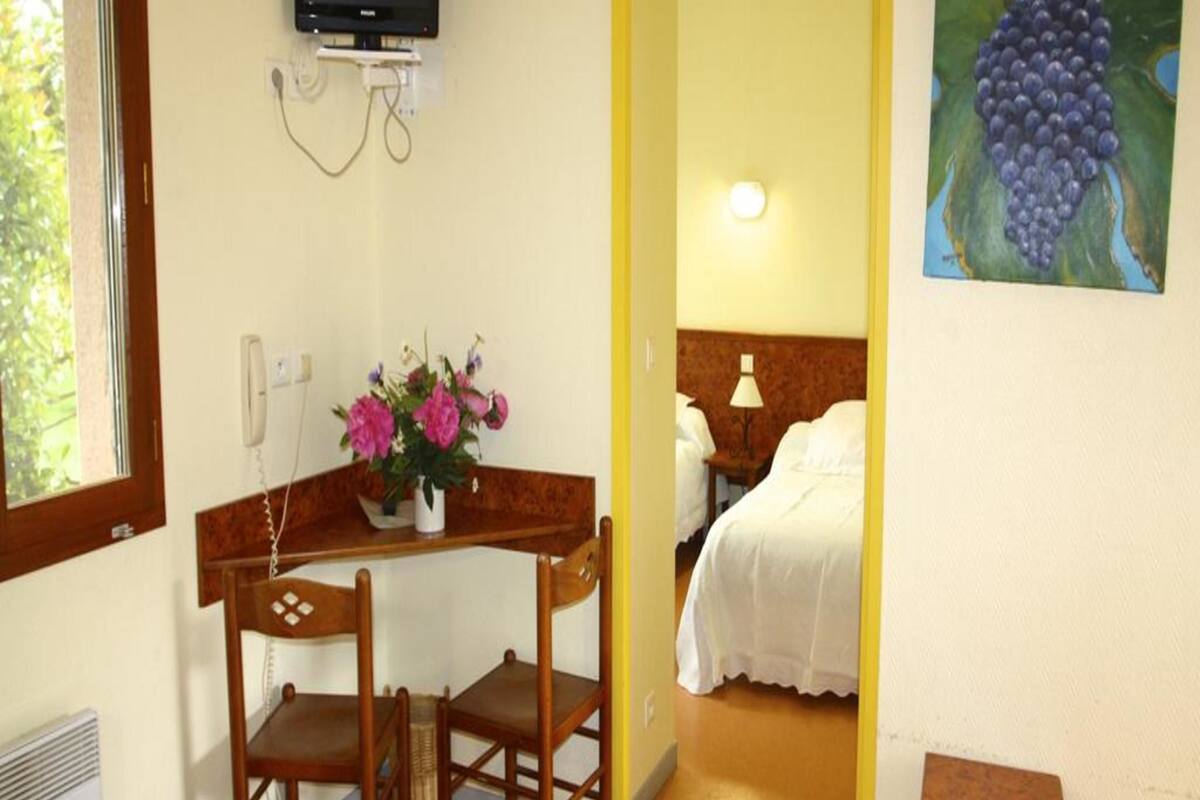 Ein Hotelzimmer mit einem Bett, einem Schreibtisch mit Stuhl, einem an der Wand montierten Fernseher und einem Wandbild mit Trauben.