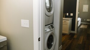 A laundry room with a front-loading washer and dryer, a countertop with a sink, and a wooden floor. - Joanna Gaines would stay here! (Sandpoint)