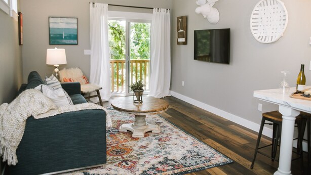 A living room with a sofa, a round coffee table, a lamp, a TV, and a dining area with a table and chairs. - Joanna Gaines would stay here! (Sandpoint)