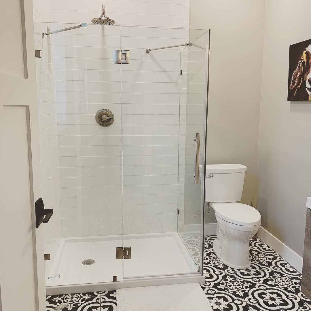 A bathroom with a glass-enclosed shower, white tiles, a white toilet, and patterned floor tiles.