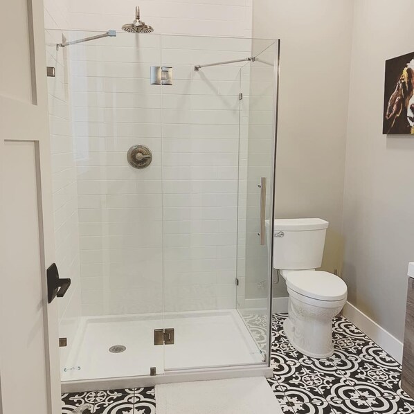 A bathroom with a glass-enclosed shower, white tiles, a white toilet, and patterned floor tiles. - Joanna Gaines would stay here! (Sandpoint)