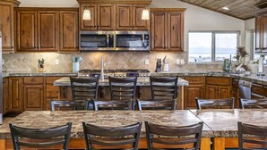 Una cocina con armarios de madera, encimera de granito, microondas integrado y una zona de comedor con sillas y una mesa.