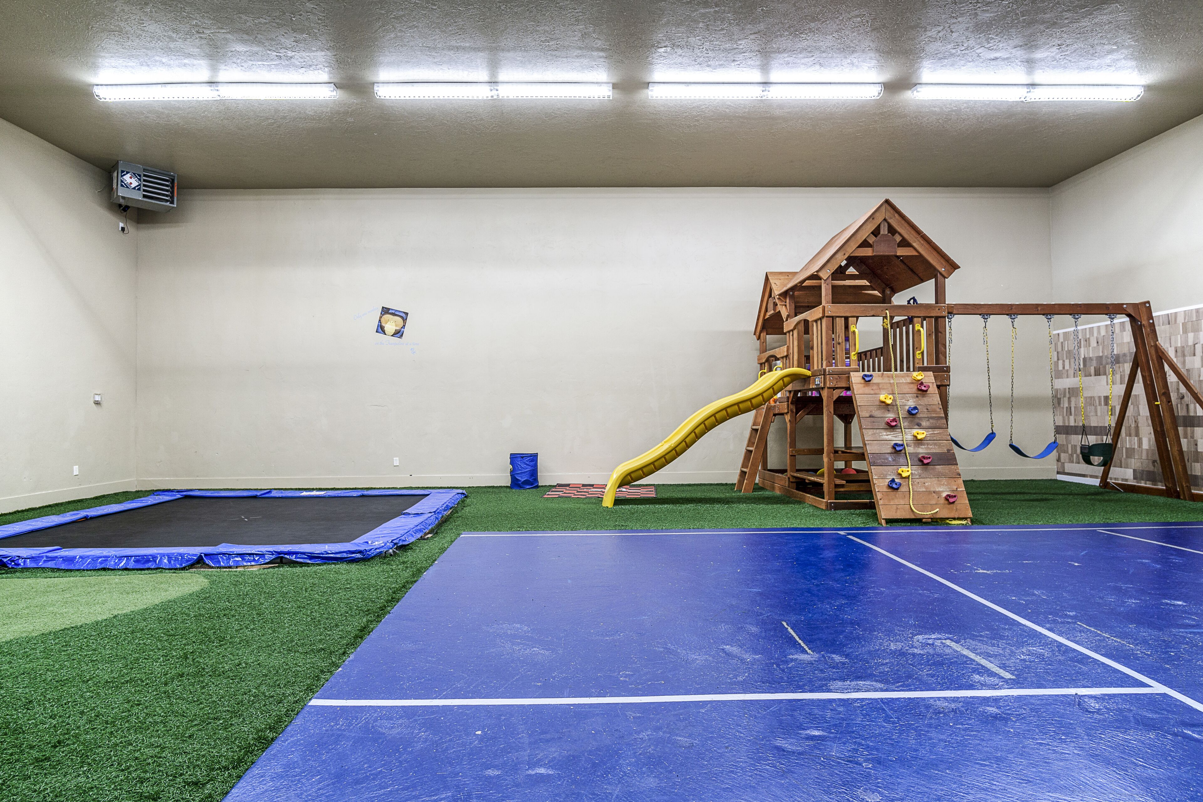 A play area with a trampoline, artificial turf, and a wooden playhouse with a slide.