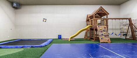 A play area with a trampoline, artificial turf, and a wooden playhouse with a slide.