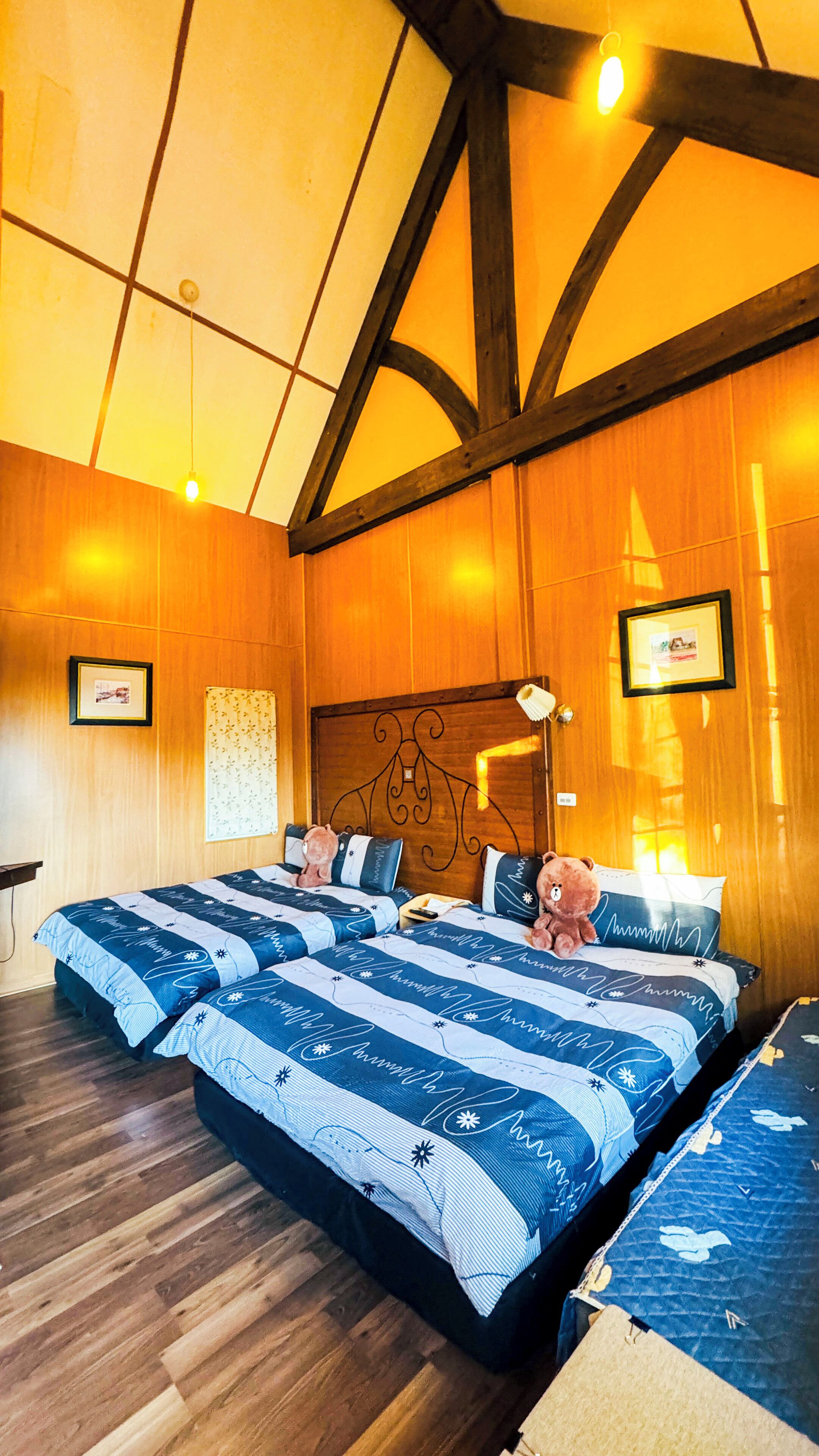 A hotel room with wooden walls, a large bed with blue bedding, a wooden floor, and a wooden ceiling with exposed beams.