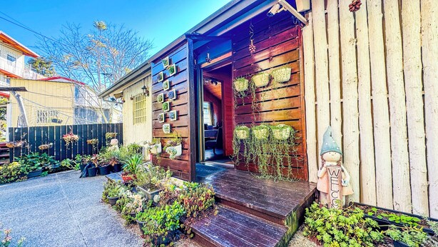 Un bâtiment en bois doté d’un porche, de plantes en pot et d’une statuette de gnome.