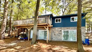 A cabin with a wooden deck and stone walls, surrounded by trees.