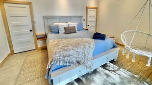 A bedroom with a bed, a hanging chair, and two doors.