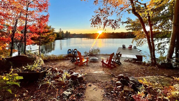 A lakeside campsite with a wooden deck, red Adirondack chairs, and a clear view of the sunset over the water.