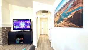 Una sala de estar con una televisión de pantalla plana, una chimenea de piedra, una estantería, un sofá y un pasillo que conduce a una puerta.