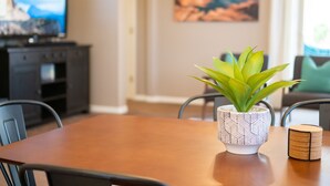 Un comedor con una mesa de madera, sillas, una planta en maceta, un televisor y un cuadro en la pared.