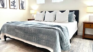 Un dormitorio con cama, almohadas, una mesita de noche, una lámpara y decoración en la pared.
