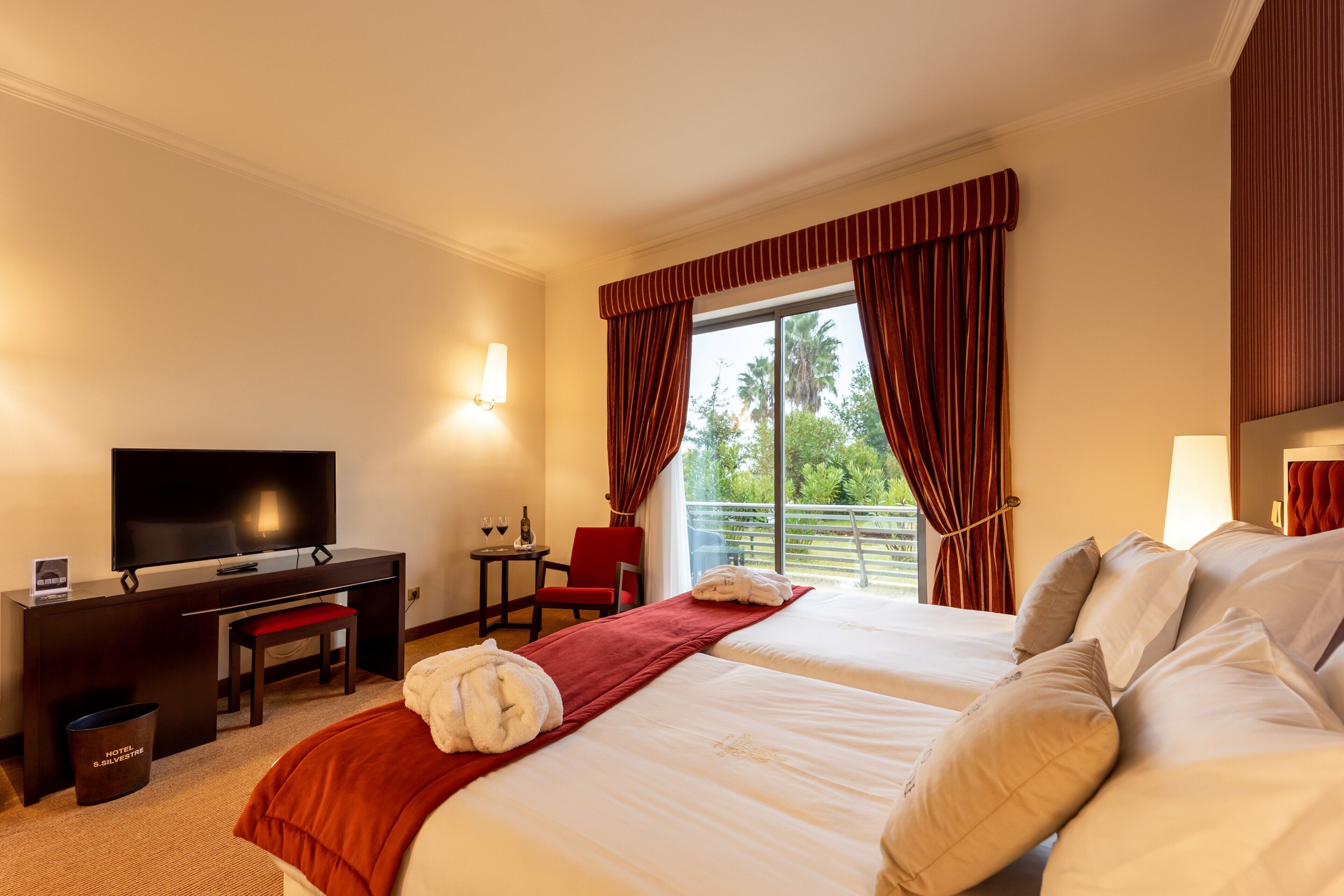 A hotel room with a bed, a desk, a TV, and a window with curtains.