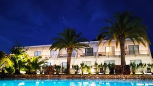A modern hotel with a pool, palm trees, and a nighttime sky.