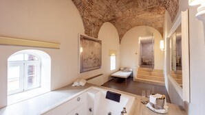A luxurious bathroom with a large bathtub, a small sofa, and a staircase leading to another room.