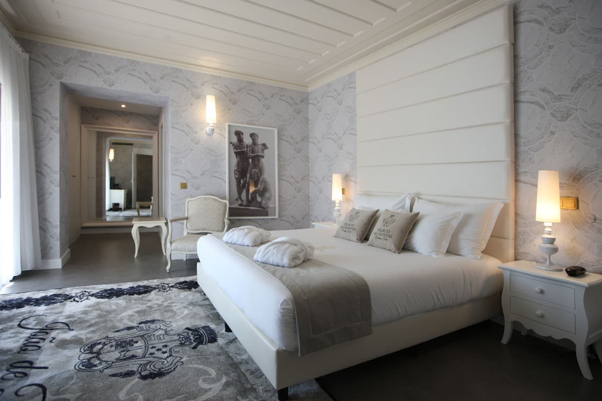 A bedroom with a large bed, bedside tables, a chair, a mirror, and a framed picture on the wall.