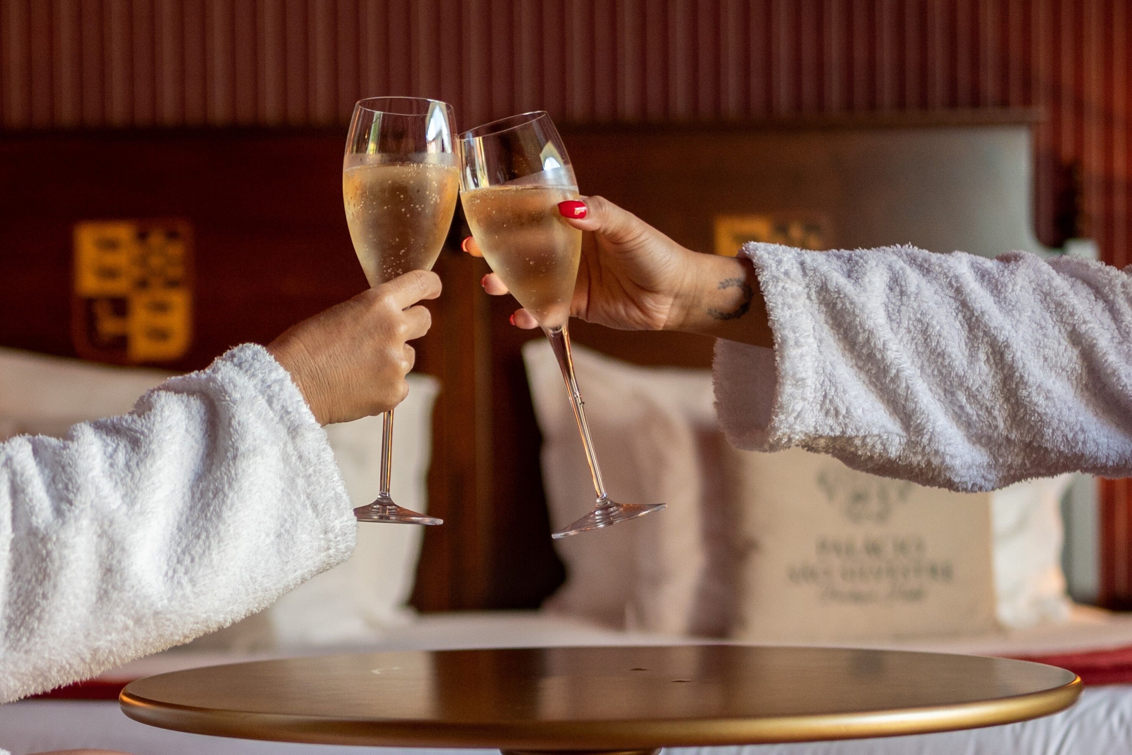 Two people toasting with champagne glasses at a round table in a room with a wooden panel wall.