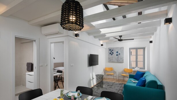 A modern living space with a dining area, a teal sofa, and a flat-screen TV. - Alla Pescheria (Rovinj)