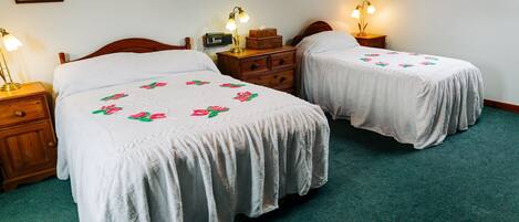 A room with two single beds, wooden nightstands with lamps, a dresser, and a small radio.