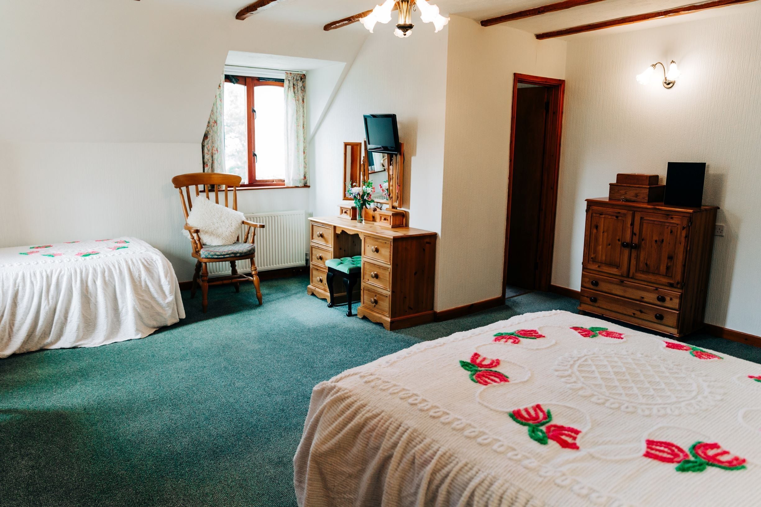 A bedroom with two single beds, a wooden dresser, a desk with a chair, and a radiator.