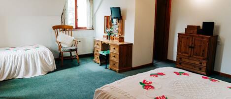 A bedroom with two single beds, a wooden dresser, a desk with a chair, and a radiator.