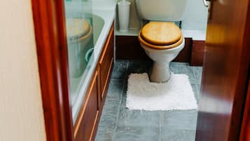 Un baño con inodoro, bañera y una pequeña alfombra en el suelo.
