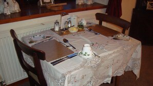 Una mesa de comedor con mantel de encaje, cubiertos y una tetera.