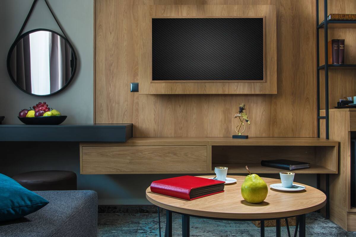 A modern living room with a round wooden table, a red book, a pear, and a cup of coffee.