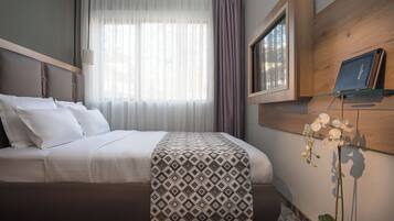 A hotel room with a bed, a window with curtains, a mounted TV, and a potted orchid.