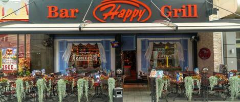 A restaurant named Bar Happy Grill with outdoor seating decorated with white flowers.