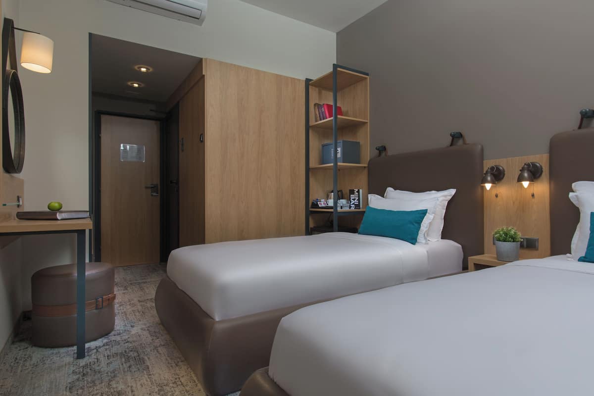 Ett hotellrum med två sängar, ett skrivbord, en bokhylla och en liten växt.