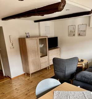 A room with a wooden cabinet, a television, a grey chair, a sofa, and two framed pictures on the wall. - Landeskrone loft maisonette - Altstadthaus / Ferienwohnungen Görlitz (Görlitz)