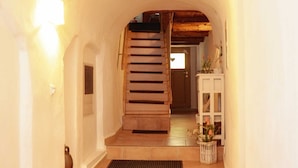 Un pasillo con una escalera de madera, un armario blanco con flores y una puerta al final.