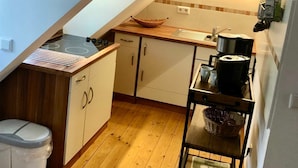 Una pequeña cocina con encimera de madera, estufa y lavabo. Hay un armario blanco con dos puertas y un cubo de basura blanco.