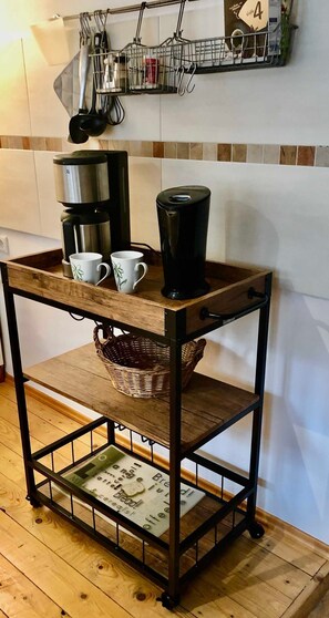 A kitchen area with a coffee station, a hanging utensil rack, and a shelf with a basket. - Landeskrone loft maisonette - Altstadthaus / Ferienwohnungen Görlitz (Görlitz)