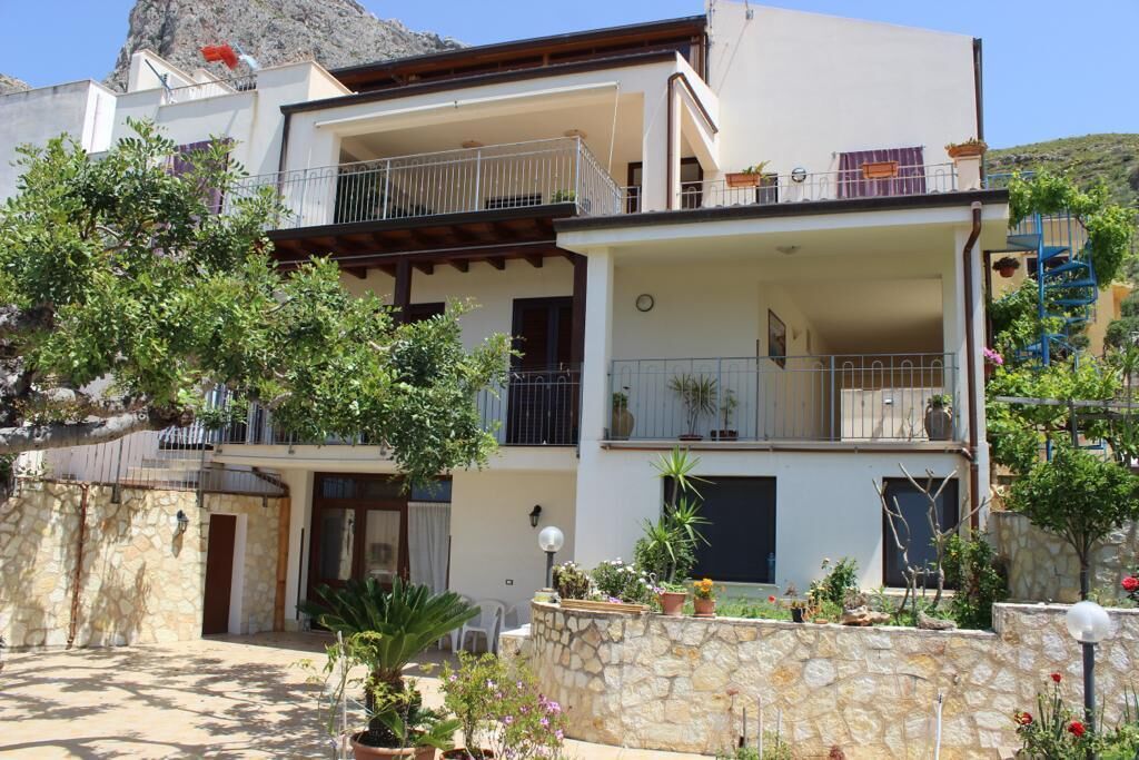 A two-story building with balconies, a stone wall, and potted plants.