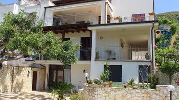 A two-story building with balconies, a stone wall, and potted plants.