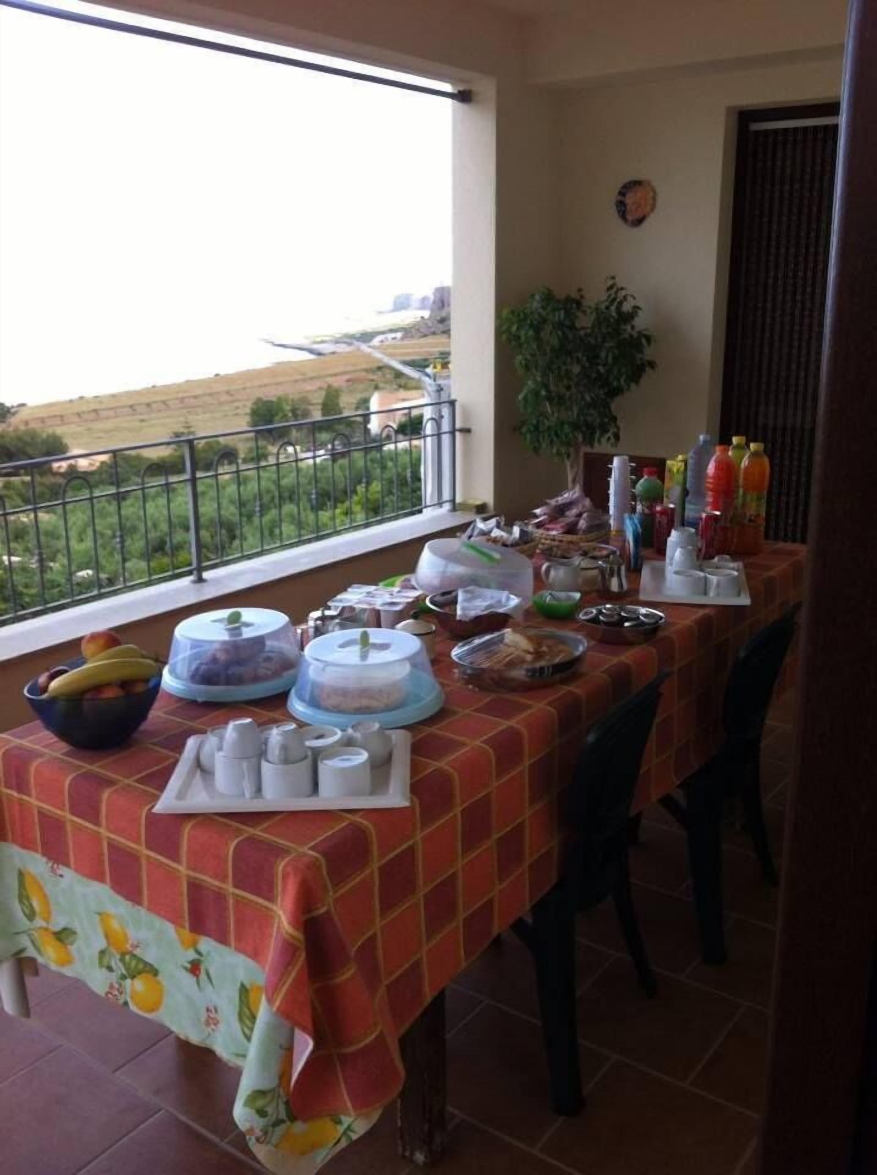 A balcony with a table set for breakfast, featuring a variety of food items and beverages.