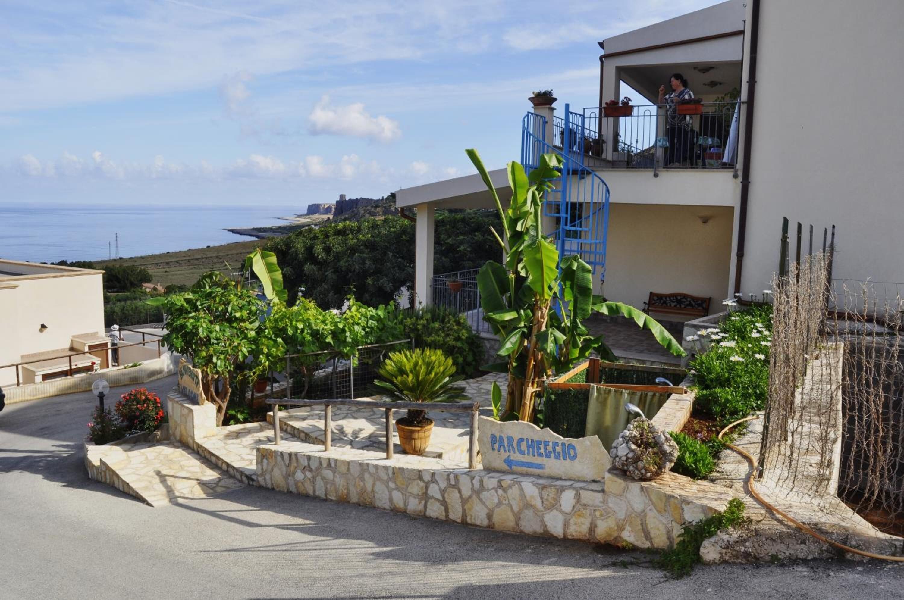 A coastal property with a stone pathway leading to a sign indicating 'Parcheggio' (parking).