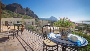 A terrace with a table and chairs, a potted plant, and a view of the sea and mountains. - Verde Mare (San Vito Lo Capo)