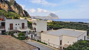 A coastal residential area with modern buildings, a rocky mountain in the background, and a clear view of the sea. - Verde Mare (San Vito Lo Capo)