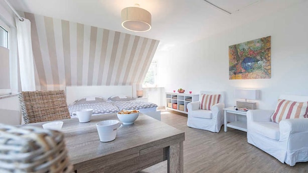 A modern living room with a wooden table, white sofas, and a striped ceiling.