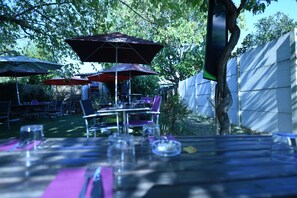 An outdoor dining area with tables and chairs, umbrellas, and a tree. - Le Juliano (Carbon-Blanc)