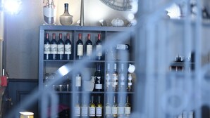 Una zona de bar con estantes llenos de botellas de vino y vasos, un reloj en la pared y un florero con flores.